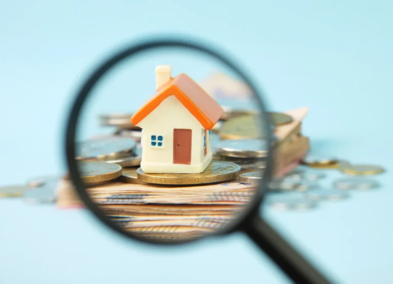Miniature house and money under a magnifying glass.