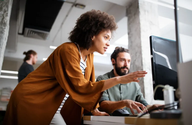 A lady pointing to a computer and talking to a men in office.